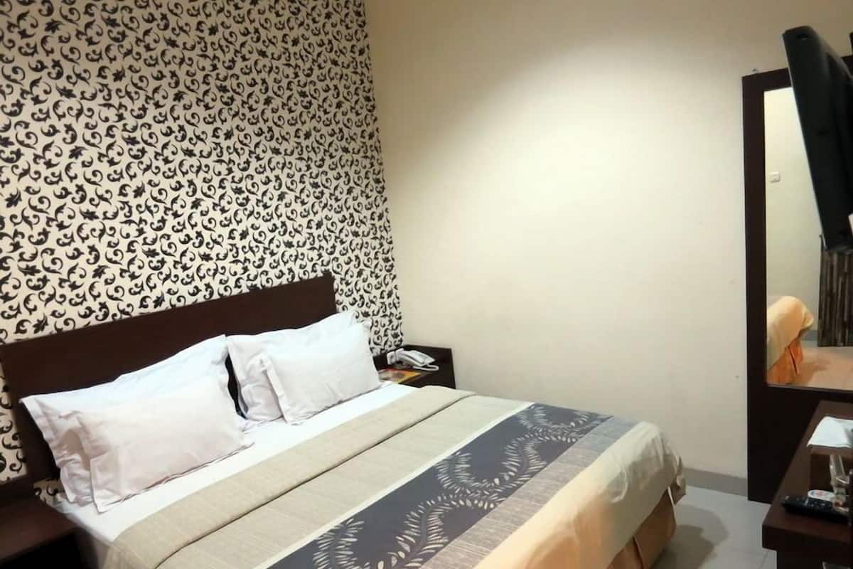 A hotel room with a bed, a nightstand, a desk, and a mirror.