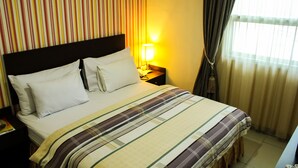 Una habitación de hotel con una cama, una mesita de noche, una lámpara y cortinas.