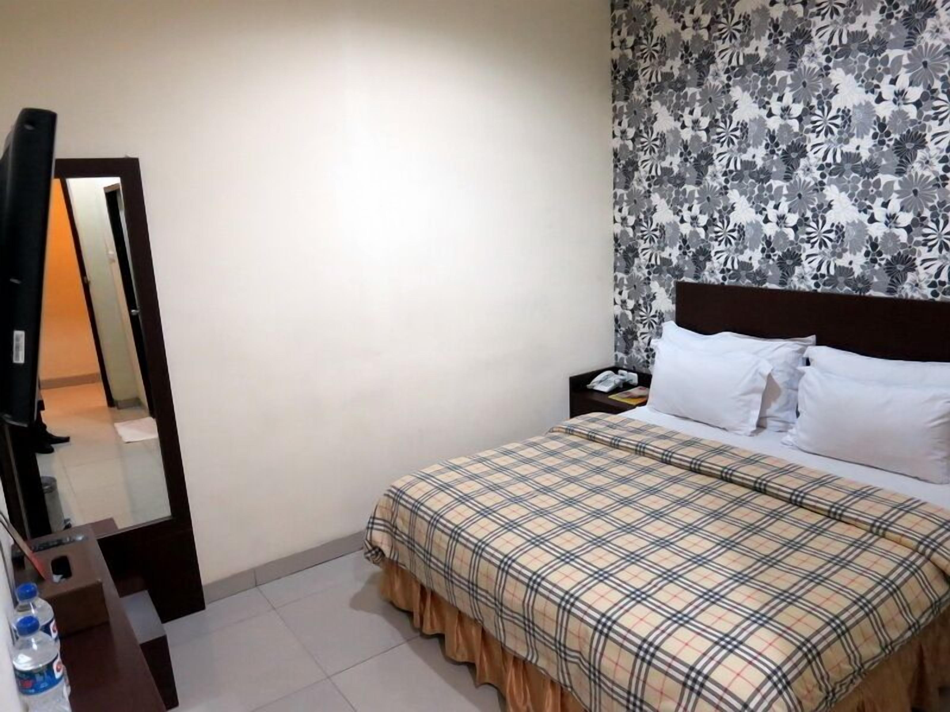 A hotel room with a bed, a nightstand, a mirror, and a wall with a floral pattern.