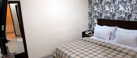 A hotel room with a bed, a nightstand, a mirror, and a wall with a floral pattern.