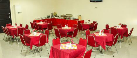 A conference room with multiple tables and chairs, a large screen, and a buffet setup.