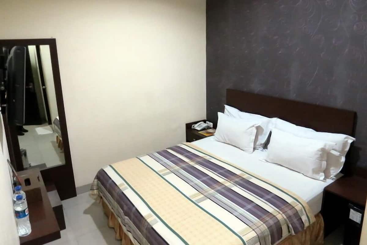 A hotel room with a bed, a nightstand, a mirror, and a water bottle.