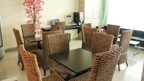 Una habitación con muebles de mimbre, una mesa, sillas, un escritorio pequeño con una computadora y una planta decorativa.