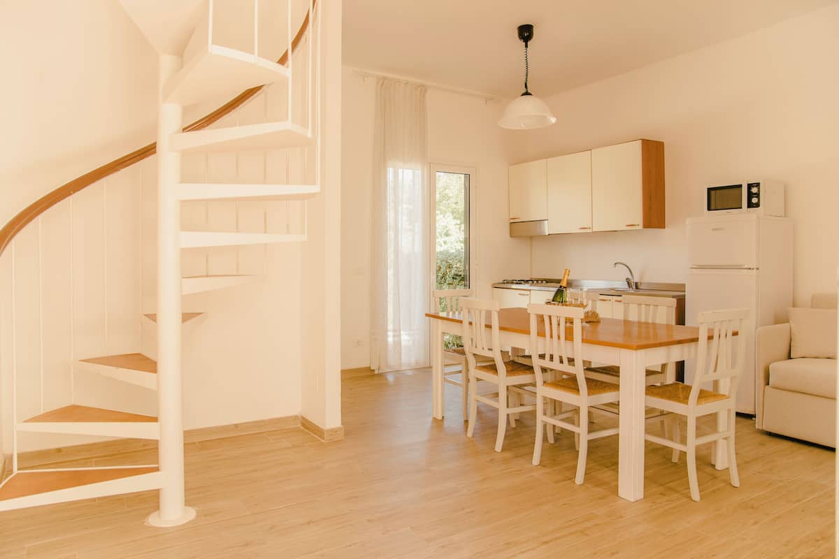 Una cucina moderna con mobili bianchi, un tavolo da pranzo in legno e una scala a chiocciola bianca.