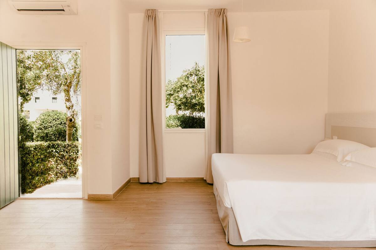 Una camera da letto con un letto, una finestra con tende, una porta che dà sull'esterno e un lampadario sopra il letto.