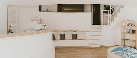 A modern, white interior with a curved bench, a wooden floor, and a staircase.