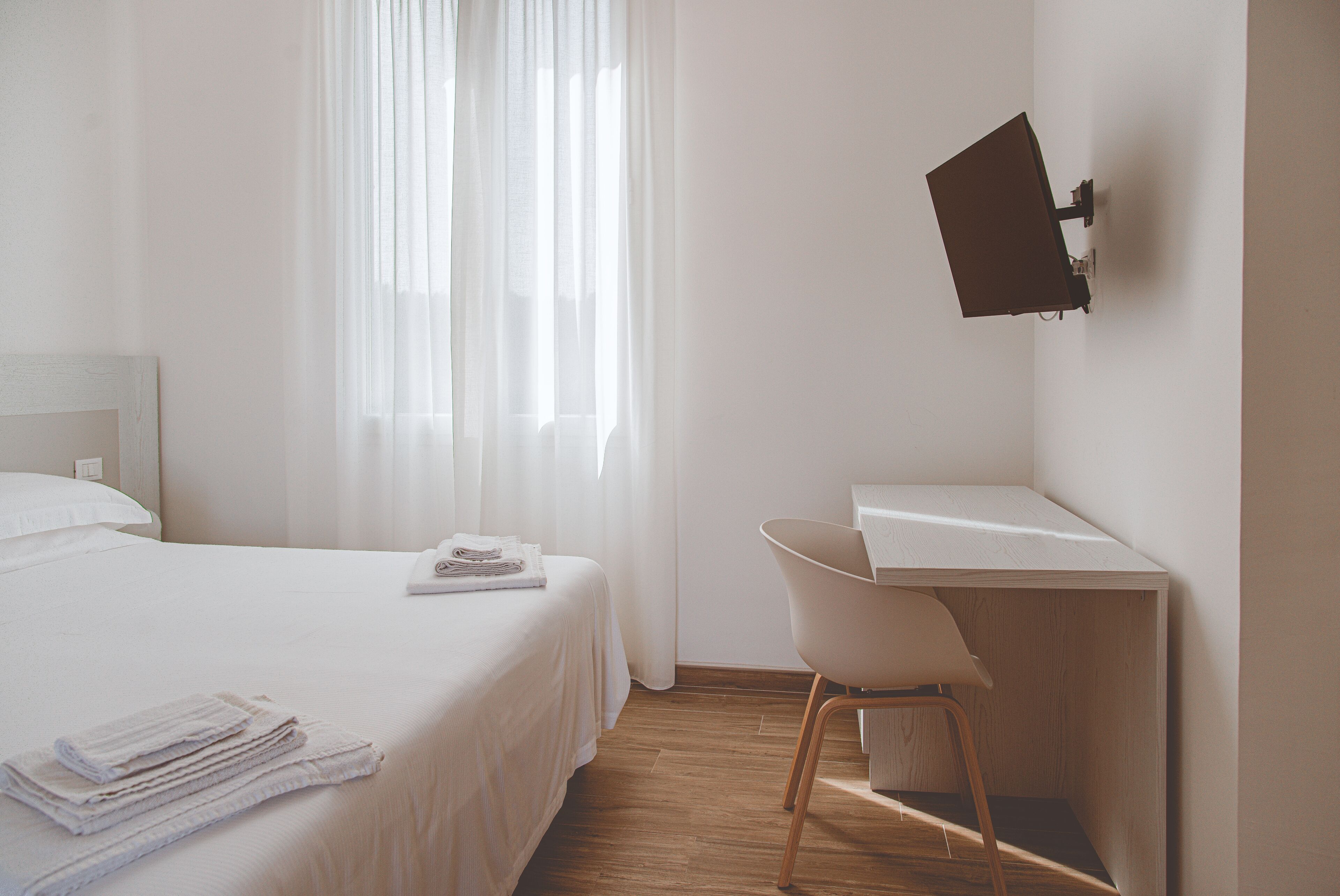 Habitación de hotel con cama, escritorio, silla y televisor montado en la pared.