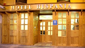 Fachada de madera del Hotel Hispania con puertas de vidrio amplias y un letrero azul con la letra 'H', que indica el hotel.
