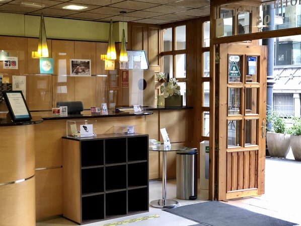 Zona de recepción con mostrador de madera, un cesto de basura y una puerta de vidrio que da al exterior.