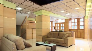 Un lobby moderno con un sofá, un sillón y una mesa de centro. Se observa una escalera y armarios de madera al fondo.