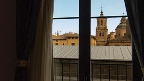Una ventana con barrotes de metal, cortinas y vistas a un edificio con una torre de campanas y techo abovedado.