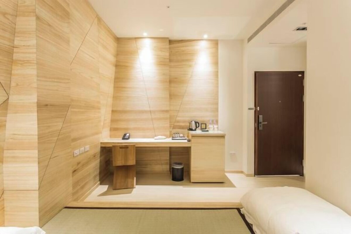 A hotel room with a wooden wall, a bed, a desk with a telephone, and a door.