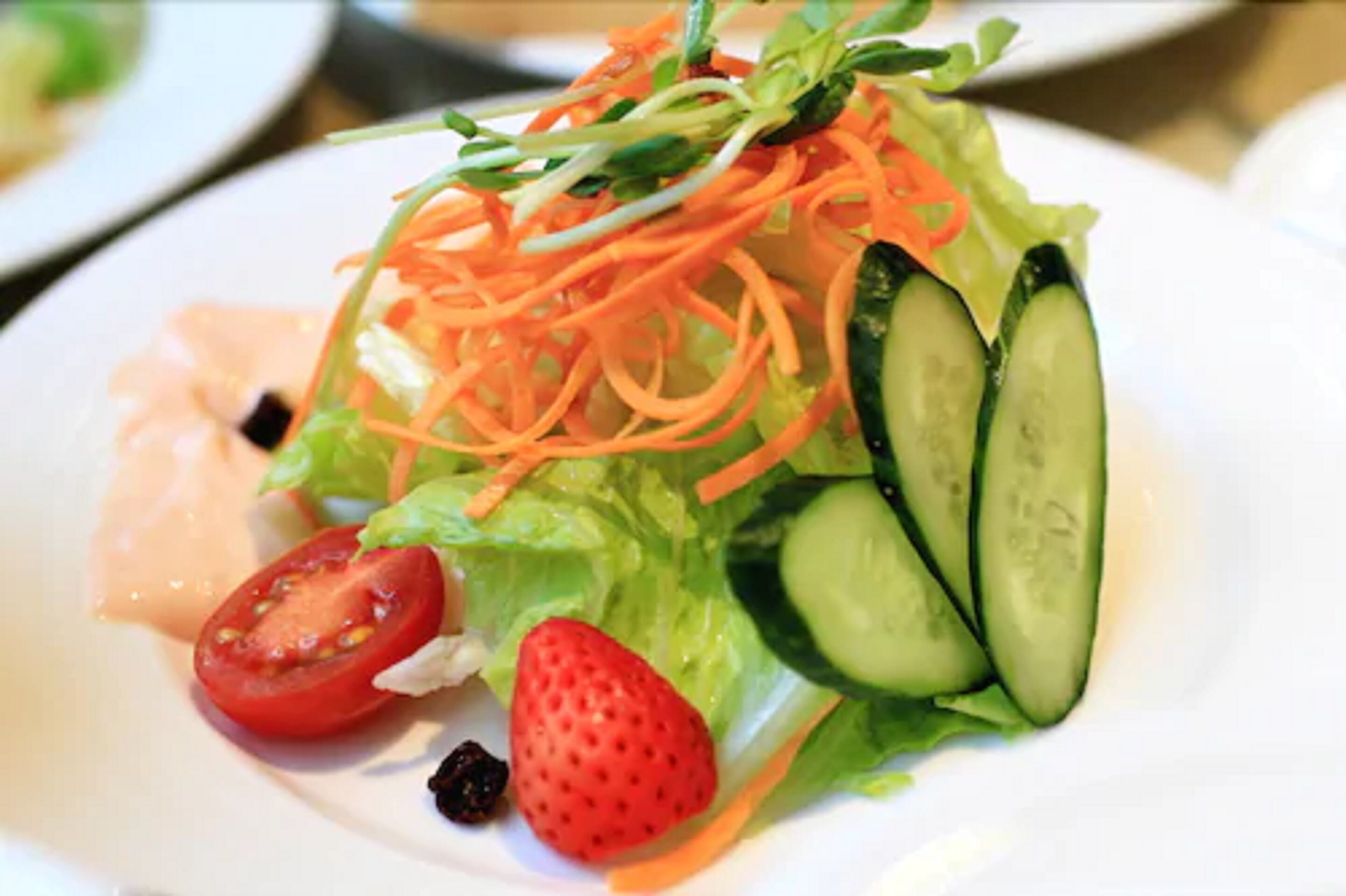 A salad with lettuce, cucumber, carrot, tomato, and blackberries on a white plate.