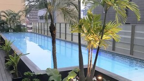 Una piscina rodeada de plantas y flores tropicales, con un edificio moderno al fondo.