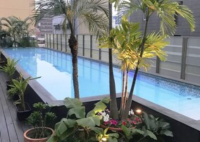 Una piscina rodeada de plantas y flores tropicales, con un edificio moderno al fondo.