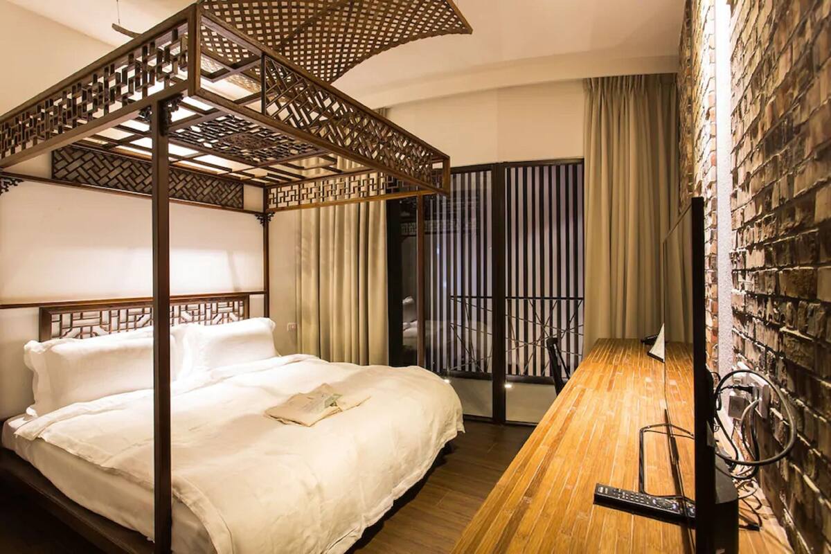Habitación de hotel con cama baldaustrada, un escritorio de madera y pared de ladrillo.