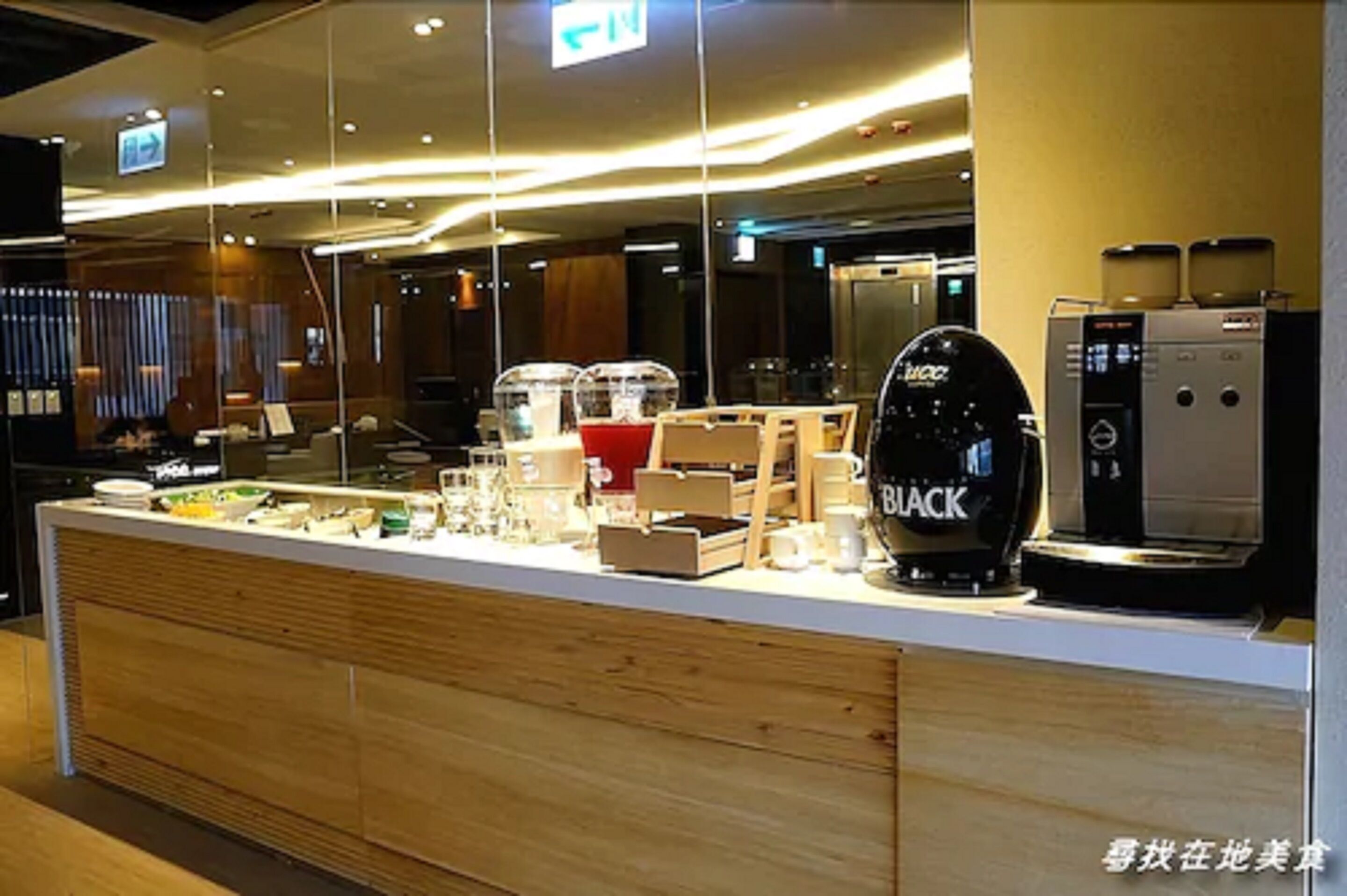 Una moderna zona de recepción de hotel con mostrador de madera, una máquina de café y una vitrina de cristal.
