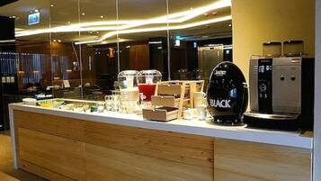 Una moderna zona de recepción de hotel con mostrador de madera, una máquina de café y una vitrina de cristal.