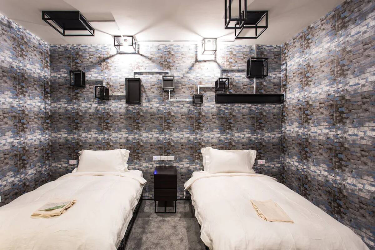 Una habitación con dos camas, una pared de ladrillo y una mesita con una lámpara.
