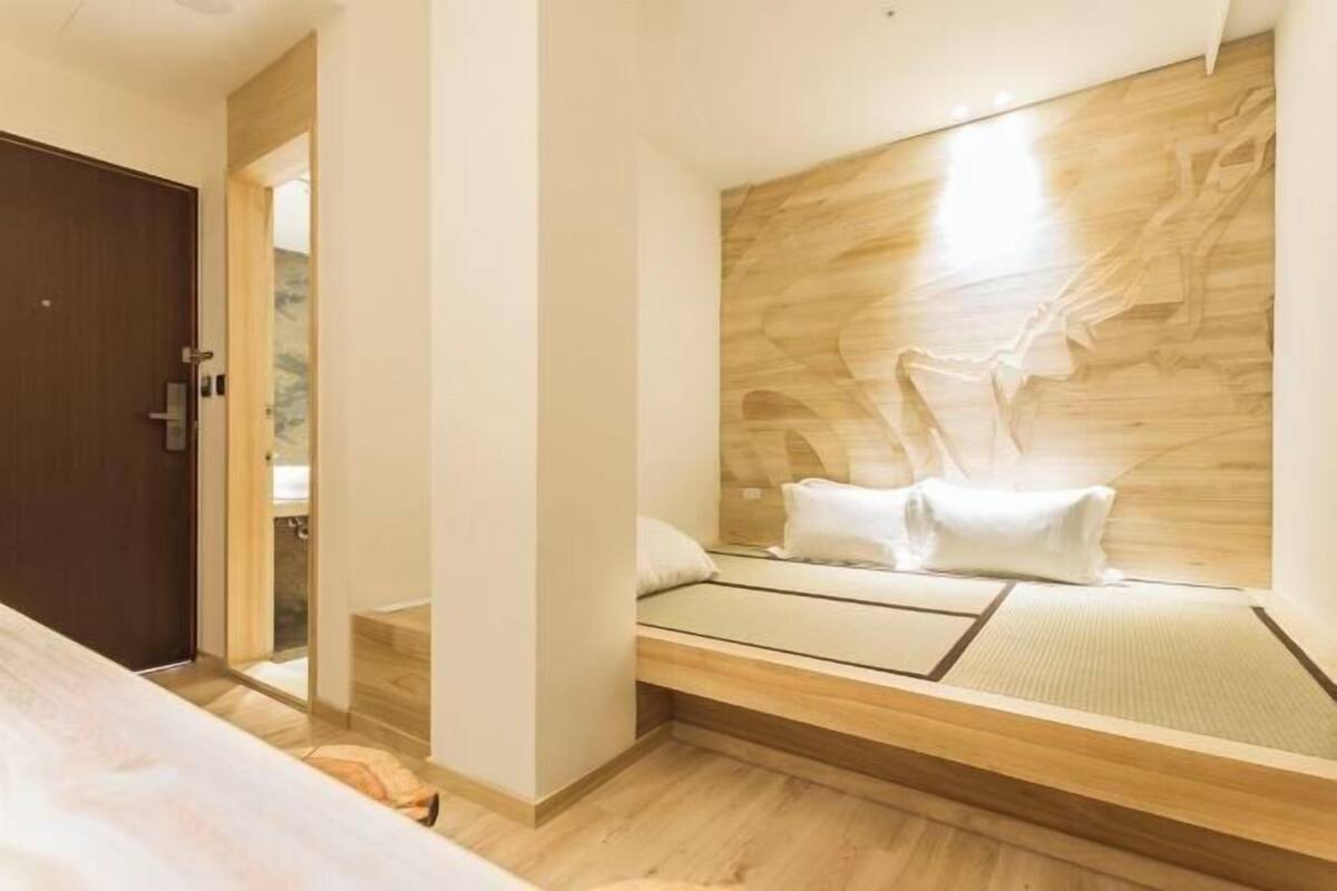 Un dormitorio moderno con cabecera de madera, cama con ropa de cama blanca y suelo de madera.