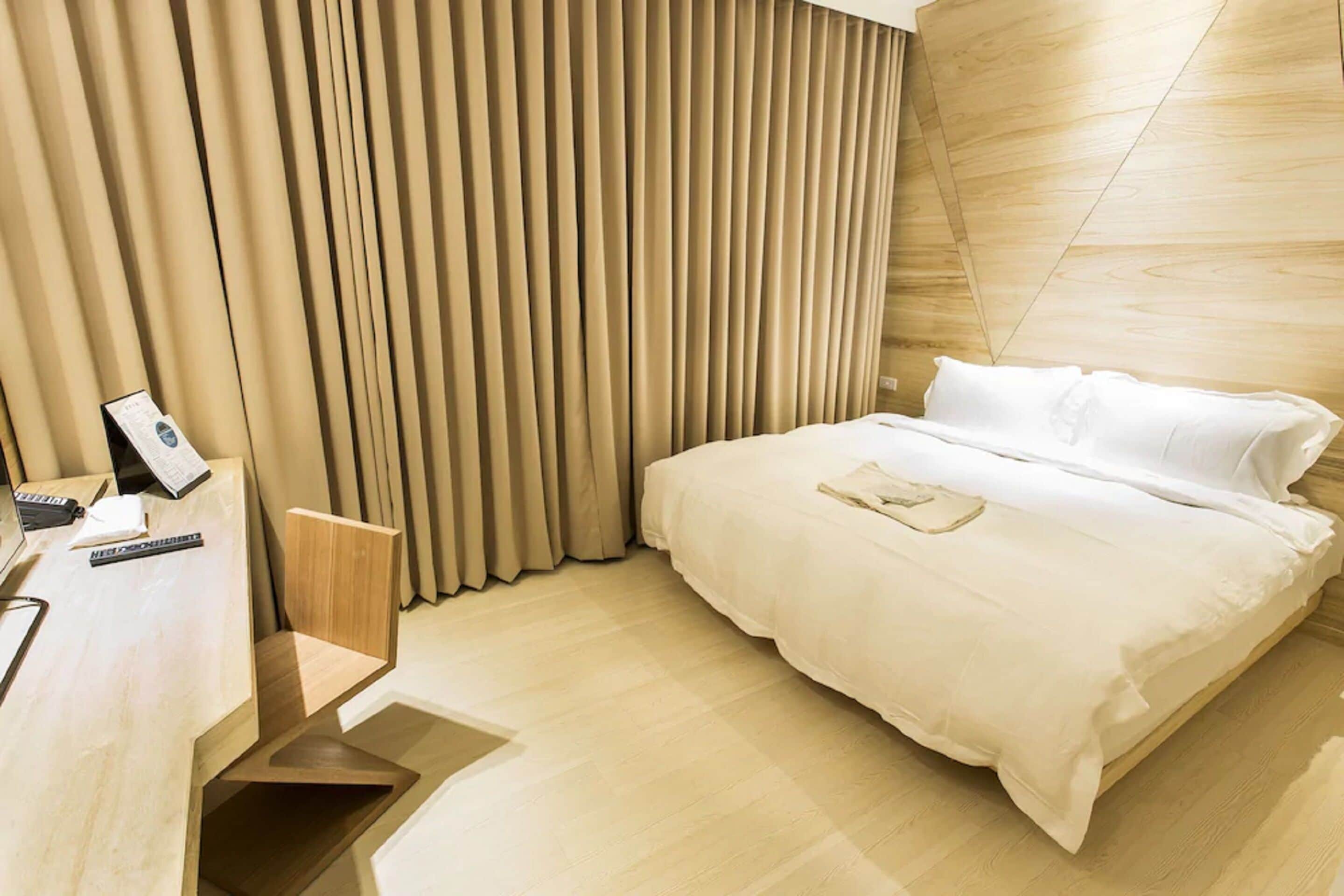 A modern hotel room with a bed, a desk, and a chair.