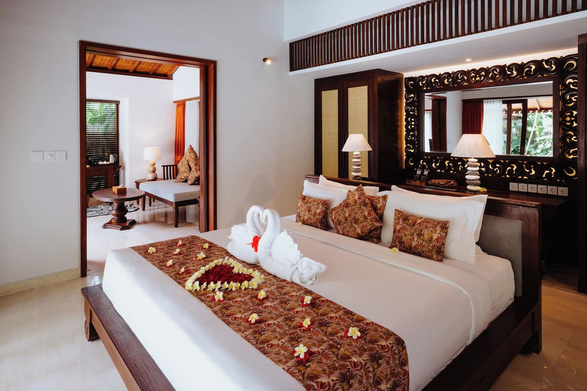 Quarto de hotel com uma cama grande, uma escrivaninha, uma cadeira, um espelho e uma janela com cortinas.