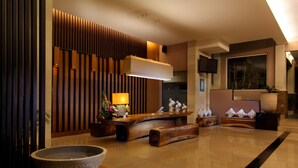Een moderne lobby met een receptiebalie, houten lambrisering, een grote stenen schaal en een flatscreen televisie die aan de muur is bevestigd.