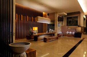 Un vestíbulo moderno con un mostrador de recepción, paneles de madera, un gran cuenco de piedra y un televisor de pantalla plana montado en la pared.