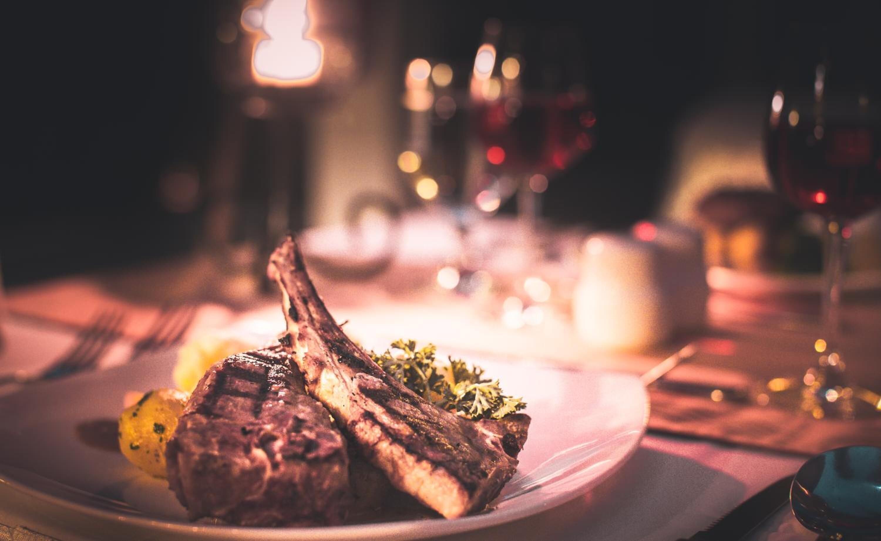 A plate with grilled meat and vegetables on a table with candles and glasses.