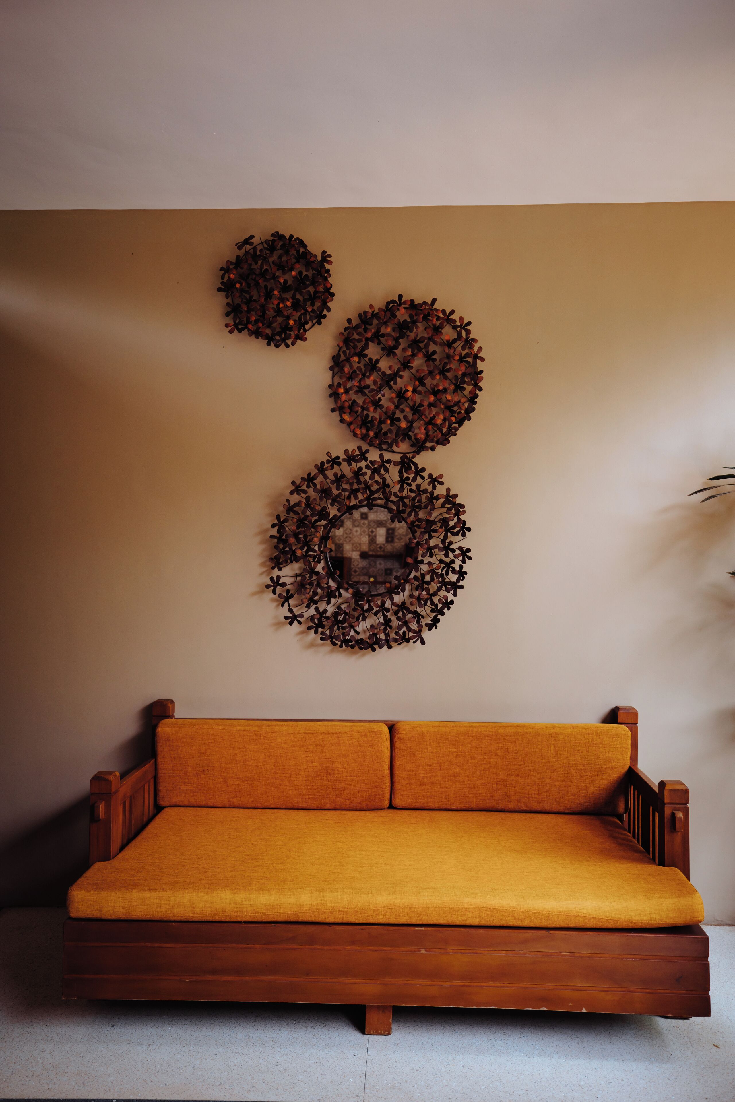 A wooden sofa with a mustard-colored cushion against a beige wall.