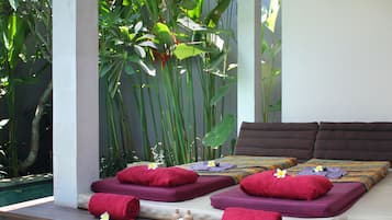 A spa area with a bed, towels, and two bowls of flowers.