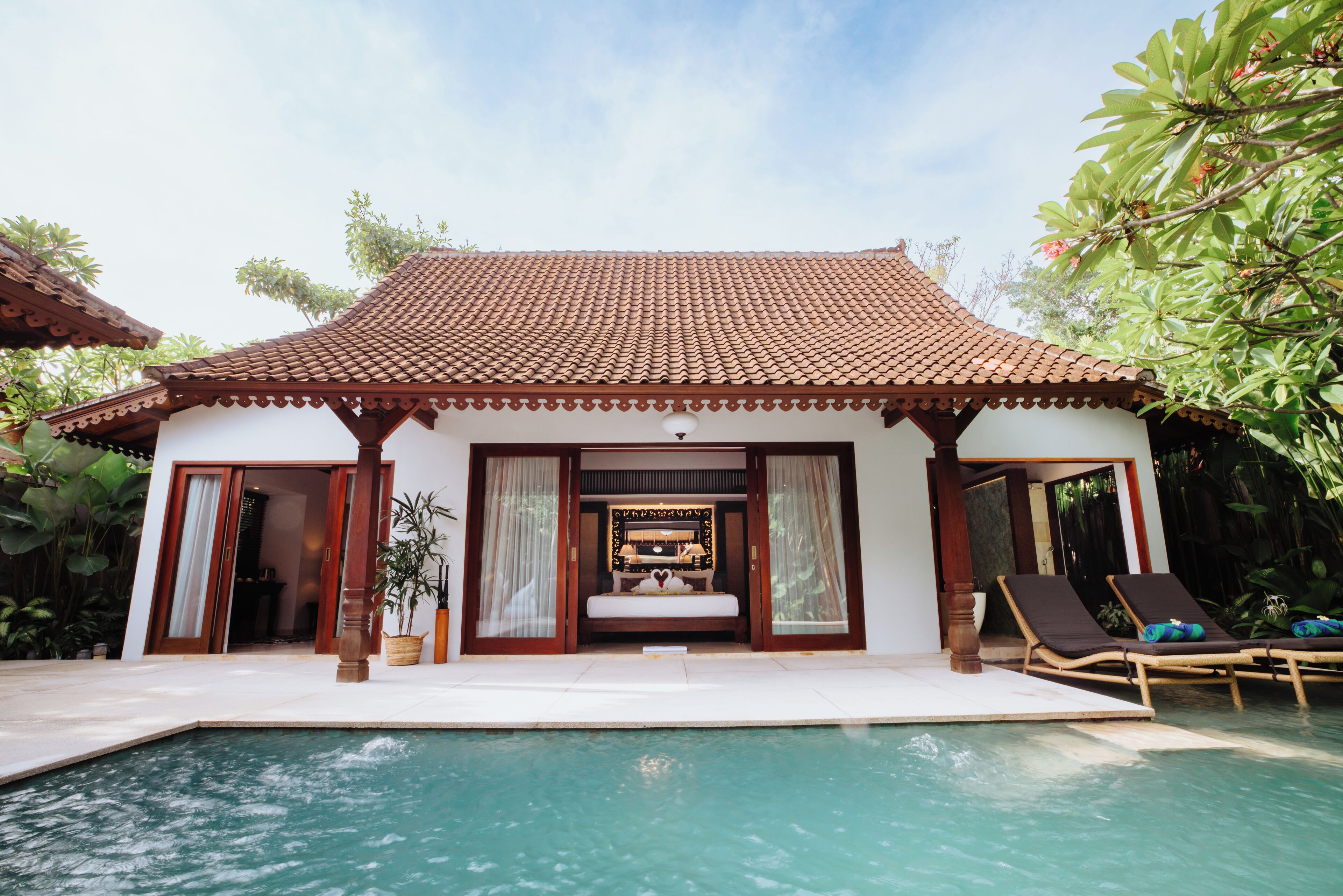 Una villa tradicional con techo de tejas, piscina y dos sillones de descanso.