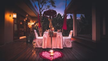 An outdoor dining area with a table set for two, surrounded by wooden flooring and decorative lighting.