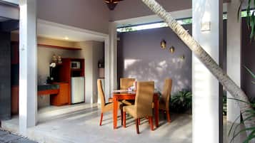 A dining area with a wooden table and chairs, a kitchen with a refrigerator and microwave, and a staircase with a decorative railing.