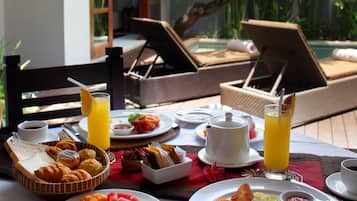 A breakfast setting with plates of food, drinks, and a poolside view.
