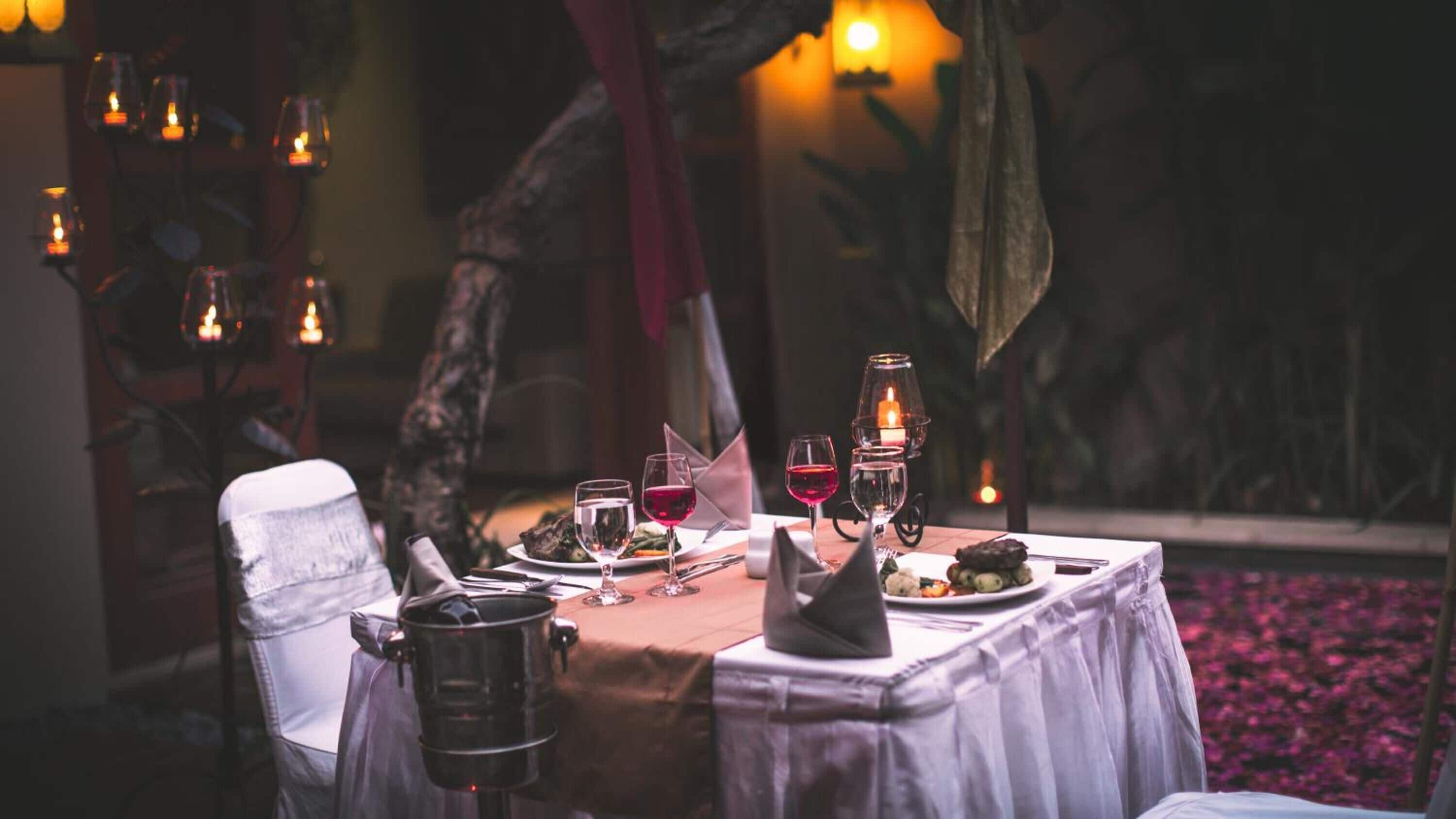 A dining table set for two with candles, wine glasses, and a pot of coffee.