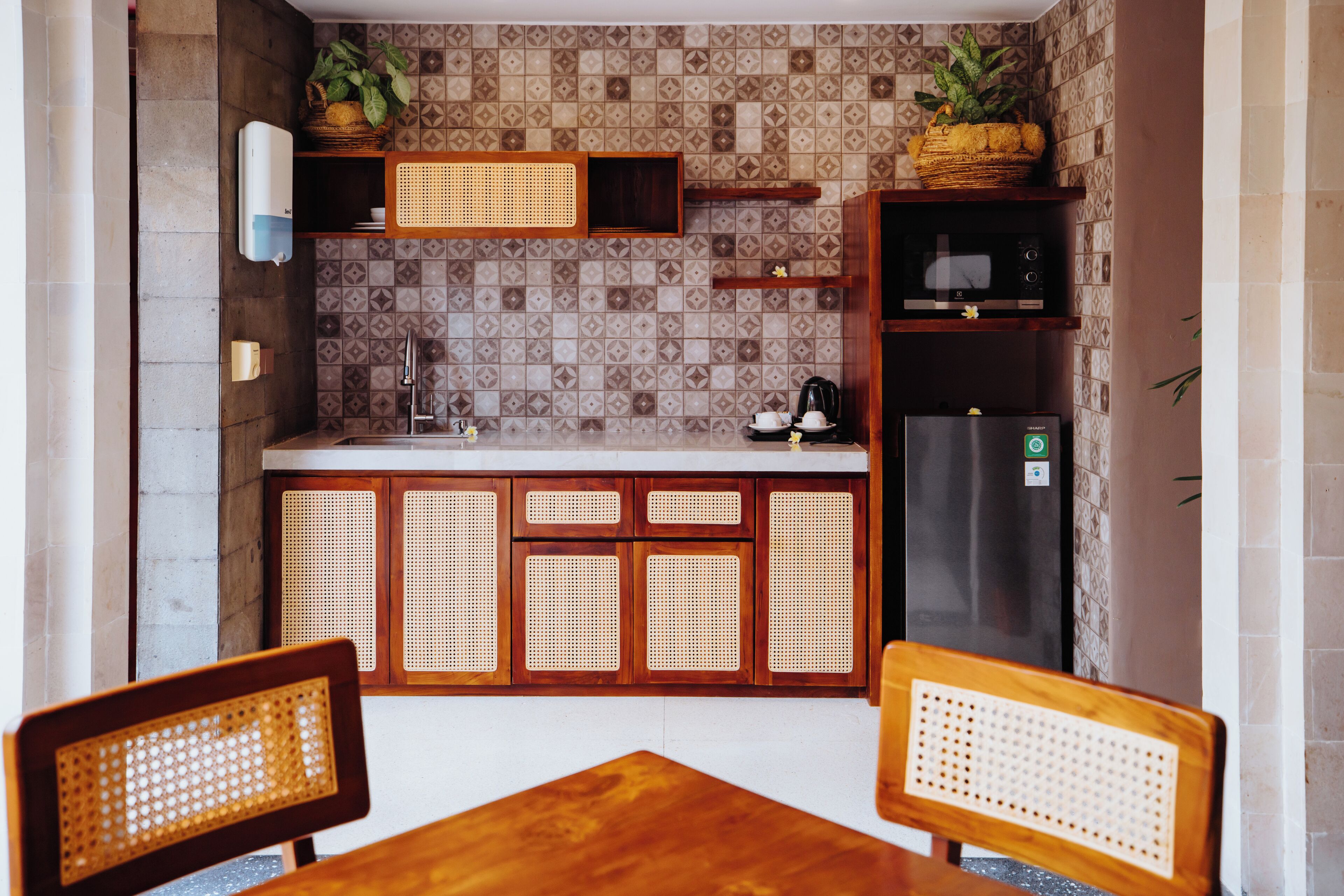 Una cocina compacta con refrigerador, microondas y pileta. Hay dos sillas de madera y una mesita pequeña.