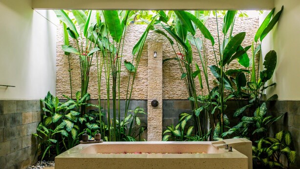 Een wellnessruimte met een groot bad, omgeven door weelderige tropische planten en een stenen muur.