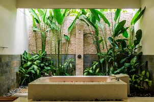 Un área de spa con una bañera grande, rodeada de exuberantes plantas tropicales y un muro de piedra.