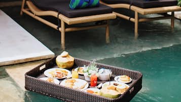 Un espace aménagé au bord de la piscine, avec deux chaises longues et un plateau flottant sur lequel sont disposés des aliments et des boissons.
