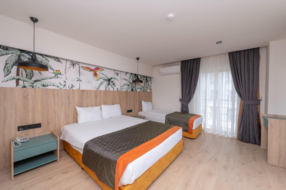 A hotel room with a large bed, a smaller bed, a desk, a telephone, and a wall with a tropical mural.