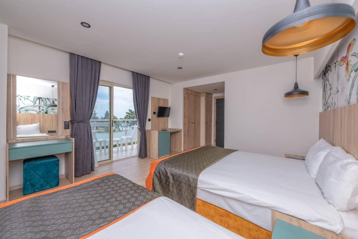 A modern hotel room with two beds, a desk, a TV, and a balcony with chairs.