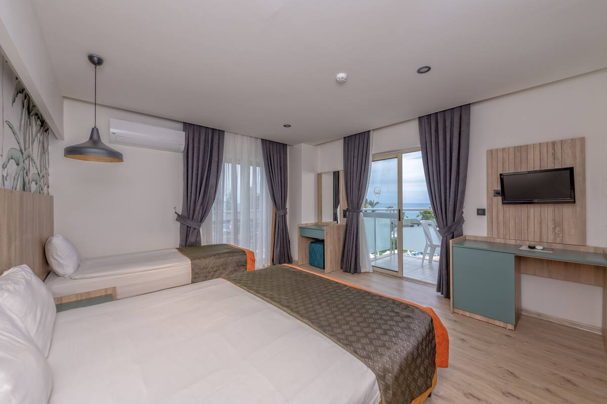 A hotel room with a large bed, a desk, a TV, and a balcony with a view.