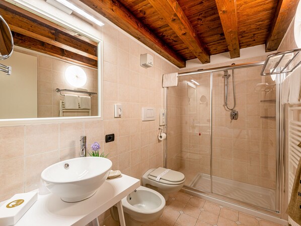 Un baño con techo de madera, un espejo grande, un lavabo, un inodoro y ducha con cerramiento de vidrio.