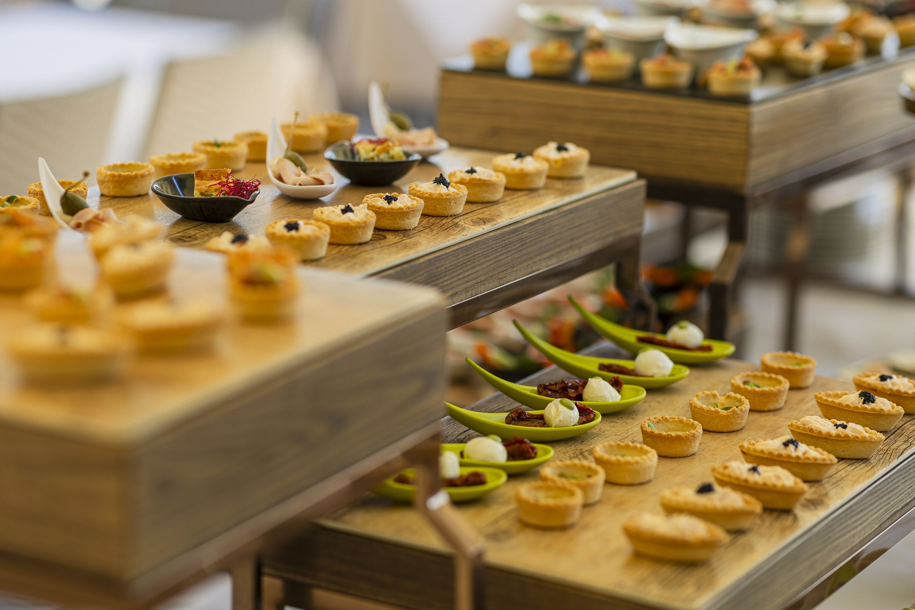 Una mesa de buffet con diversos alimentos, incluyendo mini pasteles y postres, dispuestos en tablas de madera.