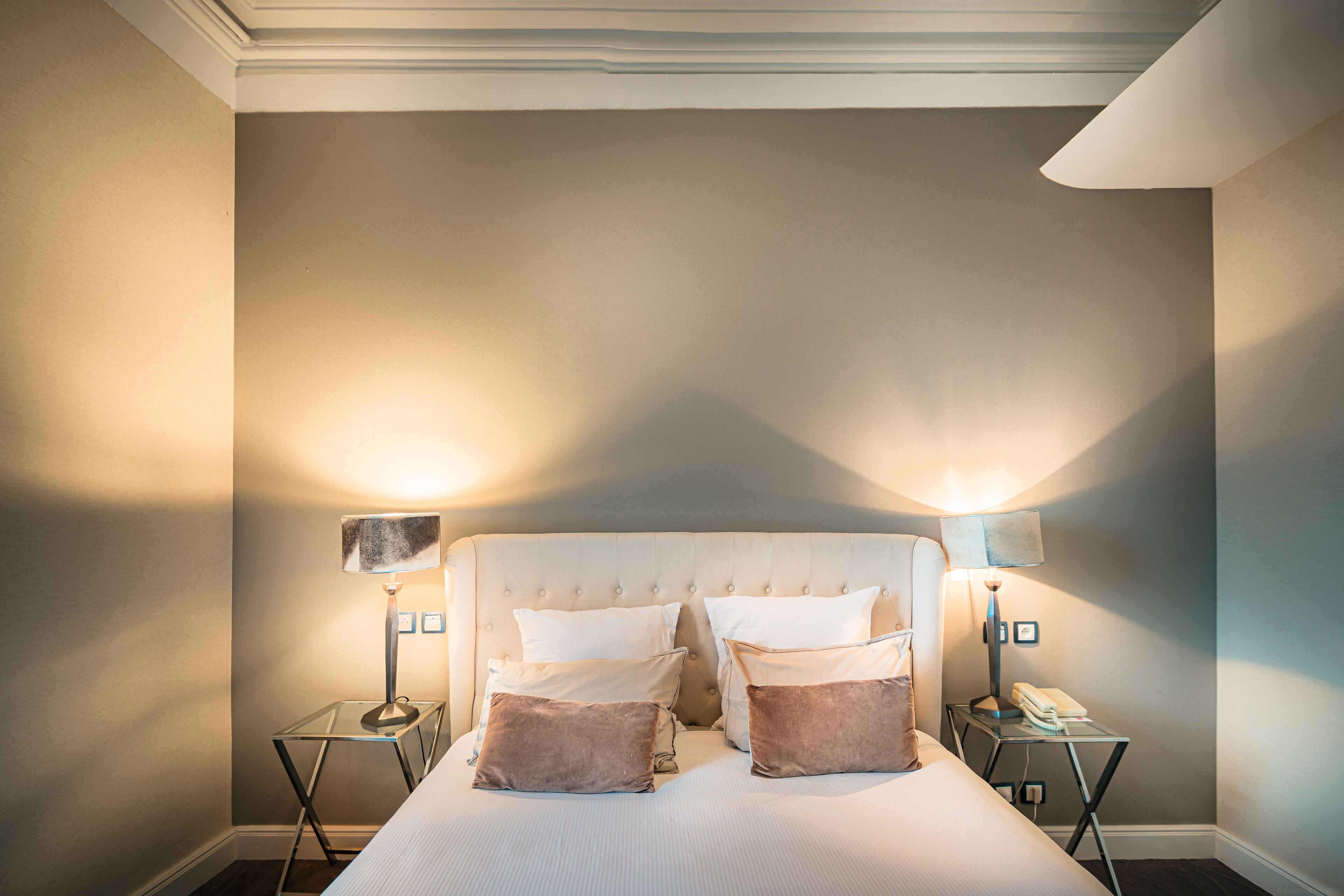 A neatly arranged bedroom with a tufted headboard, two bedside tables with lamps, and a bed with pillows.