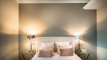 Une chambre à coucher bien rangée, avec une tête de lit capitonnée, deux tables de chevet avec des lampes et un lit agrémenté d’oreillers.