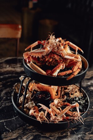 Une grande poêle noire remplie de crabes et de fruits de mer cuits, posée sur une surface en marbre.