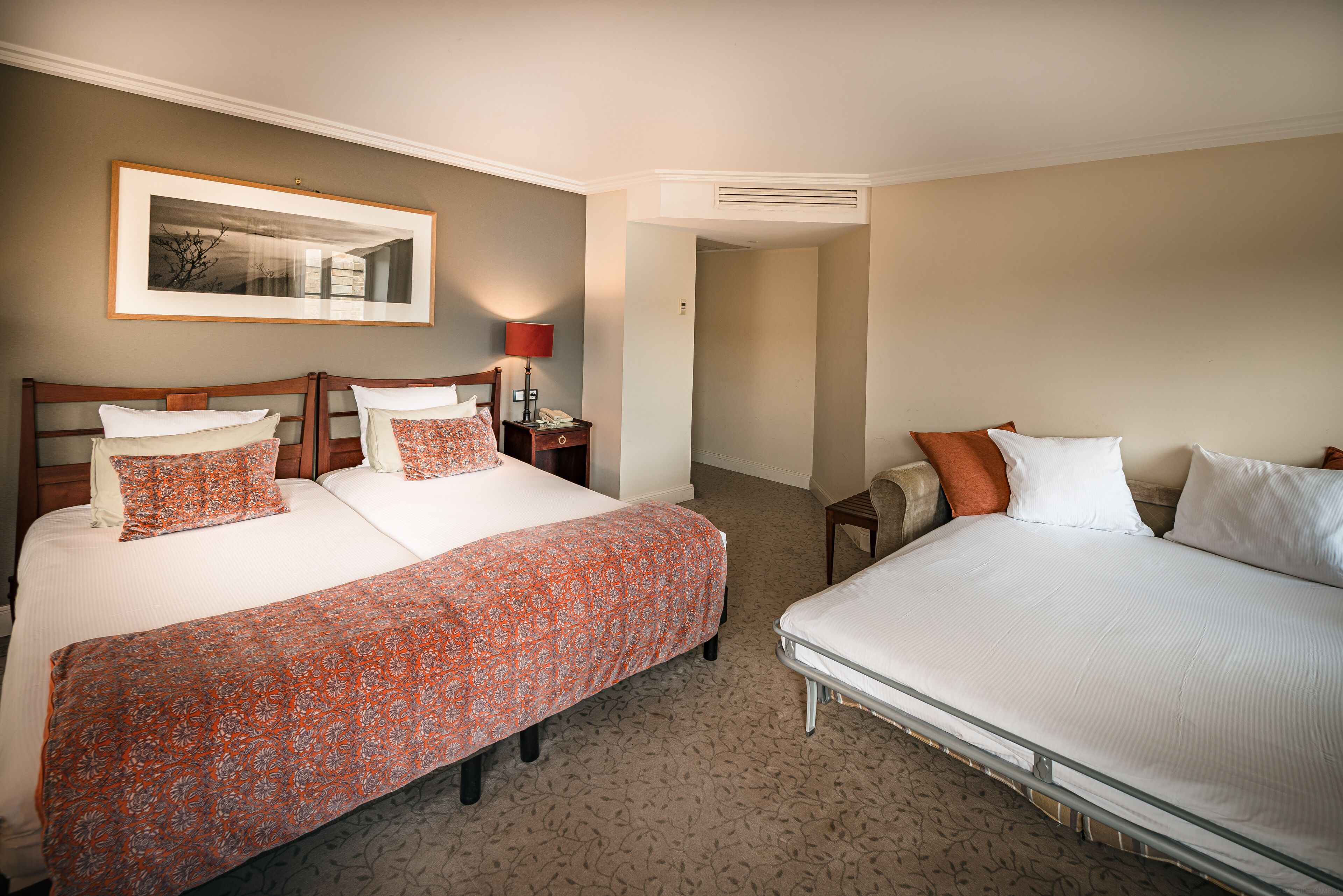 Een hotelkamer met twee bedden, een nachtkastje, een lamp en een ingelijst schilderij aan de muur.