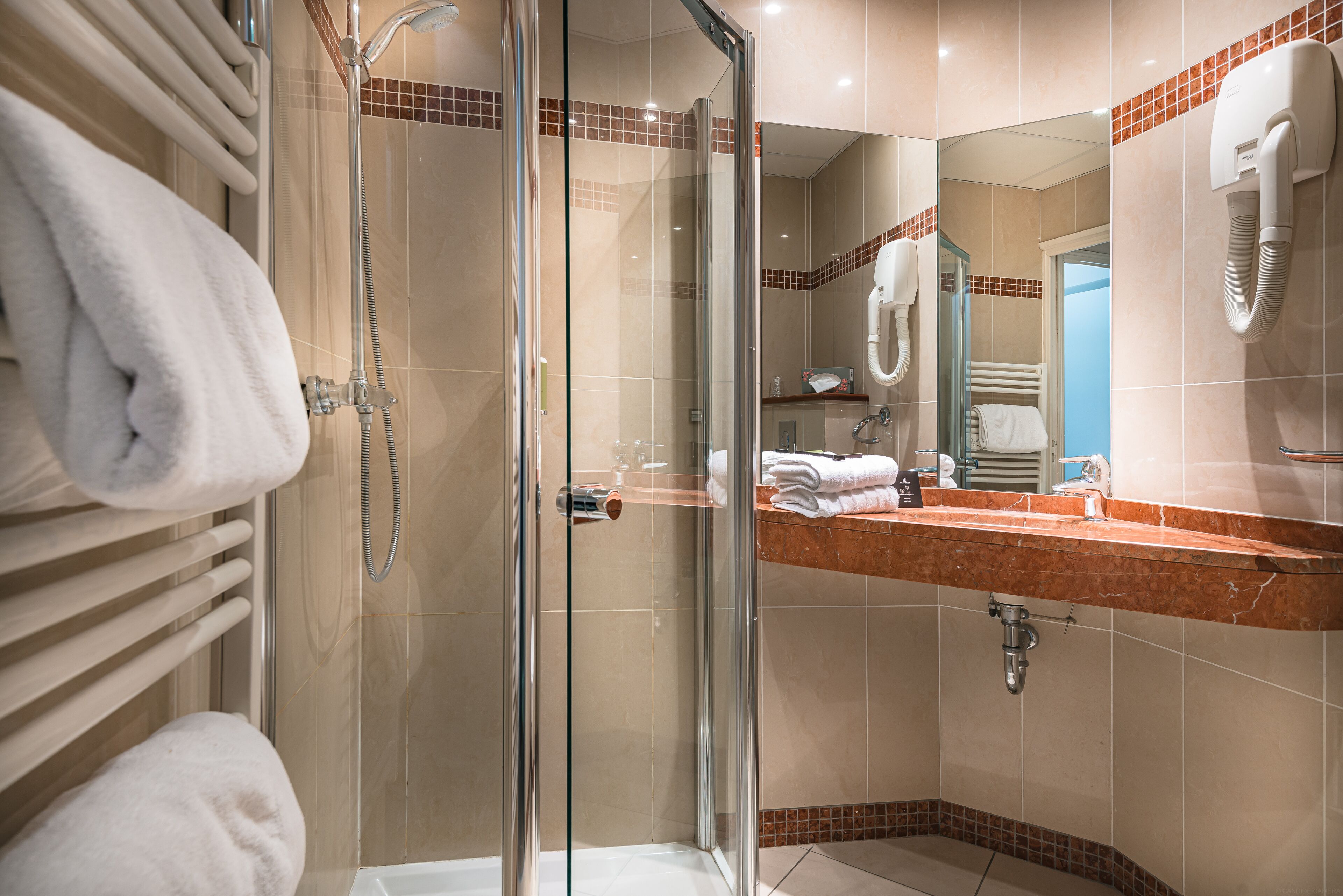 Een moderne badkamer met een douchecabine van glas, een marmeren aanrecht en een handdoekrek met netjes opgevouwen handdoeken.
